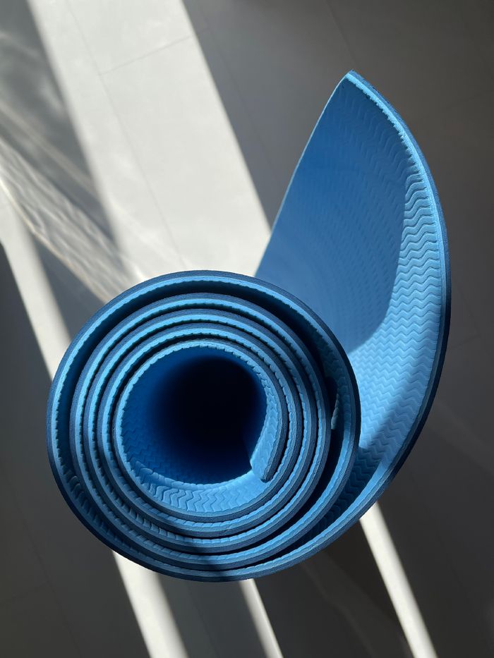 A close-up of a rolled blue yoga mat illuminated by sunlight, perfect for home workouts.