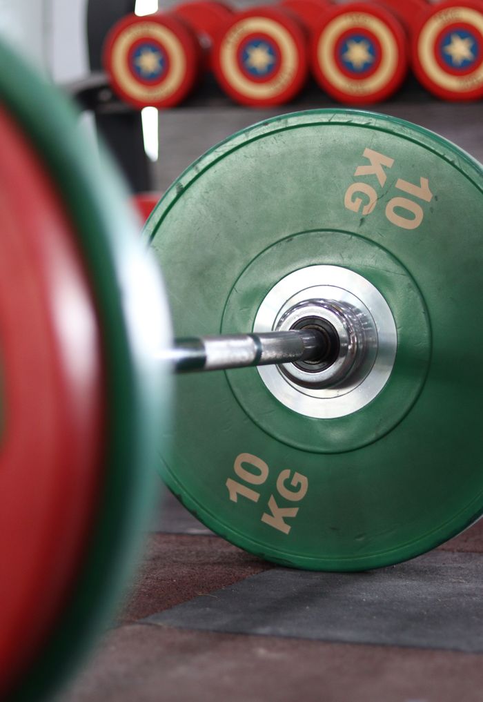 Close-up of a 10 kg green weight plate on a barbell in a gym setting, indoors.